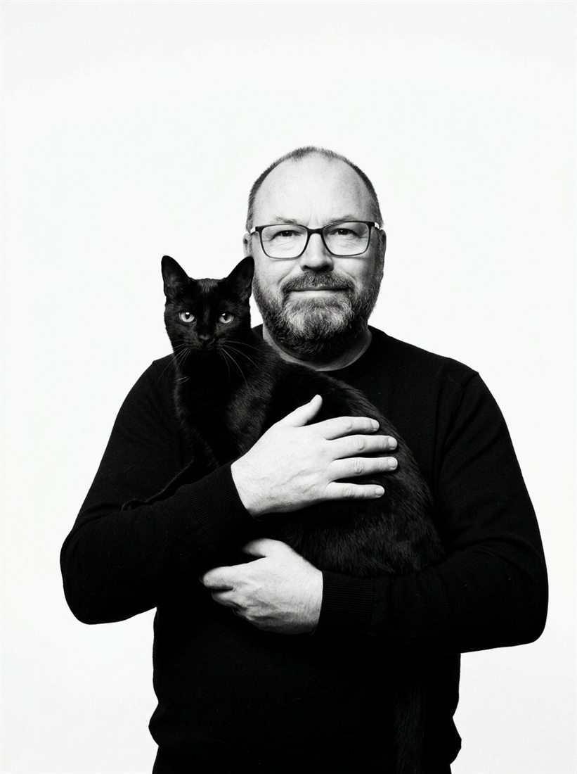 Stuart Paul Thomas holding Abbey, a black cat, against a white studio ground